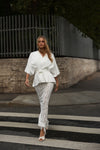 A woman walking across a city crosswalk wearing a white wrap-style top with ruffled sleeves and white lace skirt.
