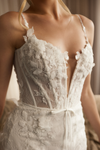 A close-up of a woman wearing a white lace bridal gown with floral appliqué, thin straps, and a deep plunging neckline.