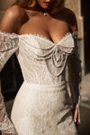Close-up of a woman wearing an off-the-shoulder lace wedding dress with a sweetheart neckline, beaded bow details, and long sheer lace sleeves.