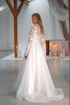 A woman wearing a white wedding dress with floral lace long sleeves and a full A-line skirt, photographed in a softly lit indoor venue with wooden beams and candles.