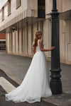 A woman wearing a sleeveless white wedding gown with a fitted lace bodice and full tulle skirt stands beside a black lamppost on a city street, looking back over her shoulder.
